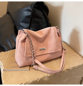 Pink matte suede shoulder bag with gold metal chain strap on textured stone surface