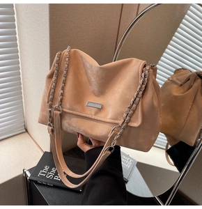 Close-up of apricot suede shoulder bag featuring a silver chain and metal brand plate