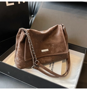 Close-up of a vintage brown leather tote bag with a metal chain strap in a premium gift box