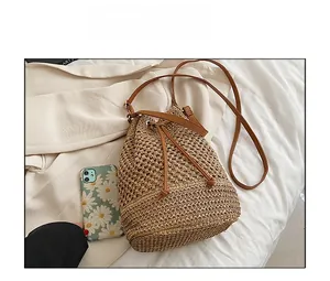 Detail view of woven straw bucket bag with brown leather drawstring and phone for scale