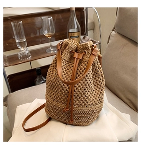 Detail view of woven straw bucket bag with dark brown leather straps for beach holidays