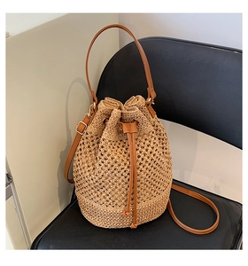 Detailed view of hollow woven straw bucket bag with dark brown leather straps and drawstring