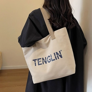 Minimalist beige canvas tote bag with blue lettering and wide shoulder straps in use