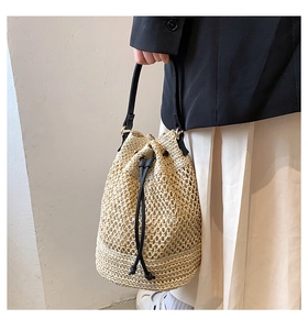 Detail of hollow woven straw bucket bag with black leather strap and drawstring closure