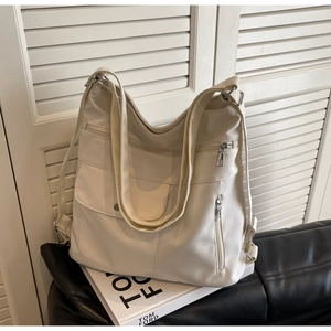 Close-up of cream white PU leather tote bag with functional pockets on black sofa