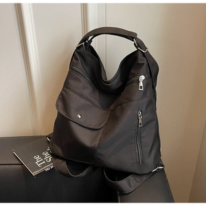 Detail of black nylon multi-pocket tote bag featuring silver hardware on leather sofa