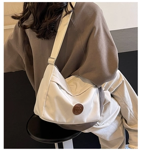 Detail of a cream-colored large canvas crossbody bag with adjustable wide fabric strap