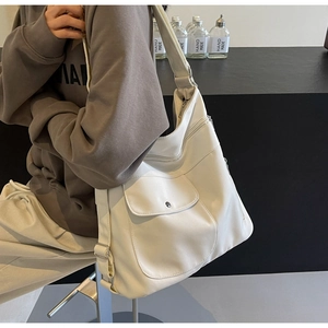 Detail view of large cream leather tote bag featuring a front pocket and wide strap