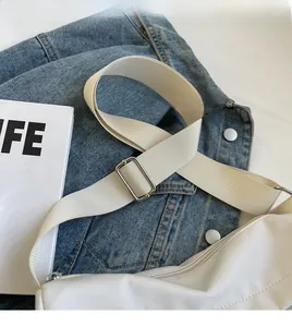 Detail of adjustable nylon strap with metal buckle on a white tote bag with fabric texture