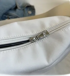 Close-up of smooth metal zipper detail on white fabric crossbody shoulder bag
