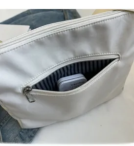 Detail of white canvas bag front zipper pocket showing striped lining and storage capacity