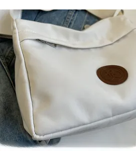 Detailed close-up of white nylon tote bag with brown leather logo and smooth zipper