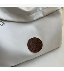 Detail of creamy white nylon tote bag showing brown leather logo patch and silver zipper
