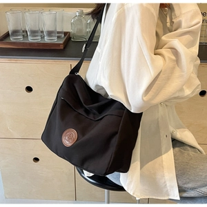 Detail of black nylon tote bag featuring a leather logo patch and adjustable strap
