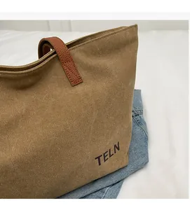 Detail of khaki canvas tote bag with brown leather handles and black TELN logo printing