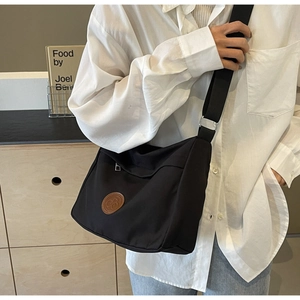 Detail of black nylon tote bag with leather logo and adjustable textile shoulder strap