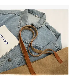 Detail of durable brown leather handles stitched onto a khaki canvas tote bag