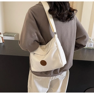 Detail of white nylon tote bag showing adjustable wide strap and circular leather patch