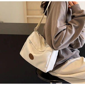 Detail view of white canvas crossbody bag with adjustable strap and leather logo patch
