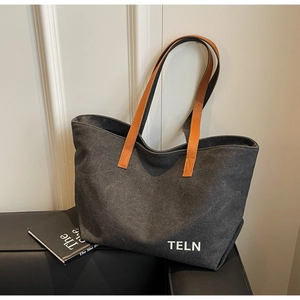 Detail of dark grey canvas tote bag with brown leather straps on a black leather sofa