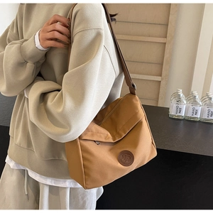 Close-up of camel nylon tote bag with round leather logo patch and adjustable strap