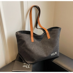 Detail of black canvas tote bag featuring orange leather handles and white logo print
