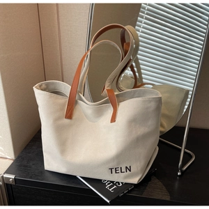 Close-up of beige canvas tote bag with brown leather handles and TELN logo detail