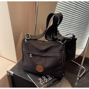 Minimalist black nylon crossbody bag with adjustable wide strap and round leather logo