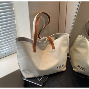 Detail of a large canvas tote bag featuring brown leather handles and TELN logo