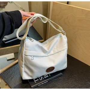 Close-up of white nylon tote bag showing front zipper pocket and adjustable strap