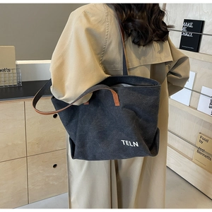 Detail of black canvas tote bag featuring brown leather handles and white TELN lettering