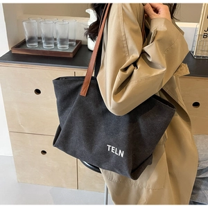 Detail of black canvas tote bag with brown leather straps and white letter print