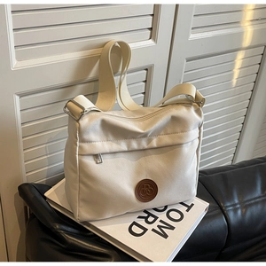 Close-up of cream nylon tote bag featuring wide adjustable strap and brown leather logo