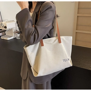 Detailed side view of white canvas tote bag with brown leather straps and TELN print