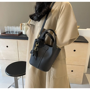 Black pebbled leather bucket bag with gold hardware and elephant charm shown crossbody
