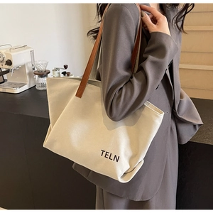 Detail of canvas tote bag with brown leather handles and black logo on a beige surface