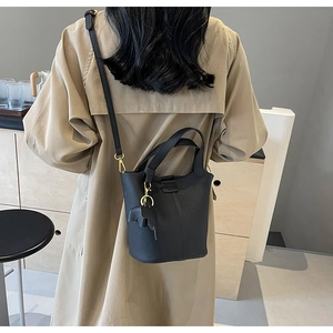 Detail of black pebbled leather bucket bag with cute elephant charm on a khaki trench coat