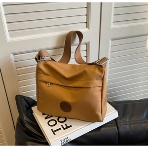Detail of tan nylon tote bag showing front zip pockets and wide woven shoulder strap