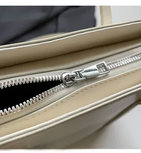 Close-up of smooth silver metal zipper and fine leather stitching on off-white tote bag
