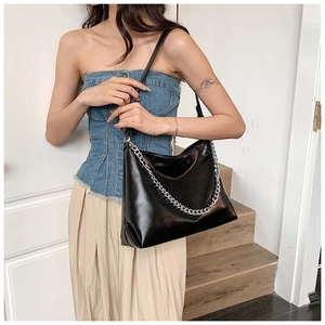 Detail of black glossy leather tote bag featuring a chunky silver chain and adjustable strap