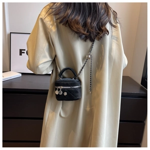 Détail d'un mini sac bandoulière matelassé noir avec chaîne dorée et breloque fleurie