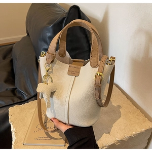 Detail of off-white lychee leather bucket bag with brown strap and elephant charm