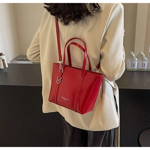 Model view of a red glossy tote bag featuring metallic hardware and a detachable strap