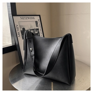 Detail of black leather shoulder bag showing wide strap with silver metal studs