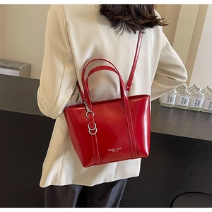 Red patent leather tote bag with silver buckles worn over a beige suit blazer
