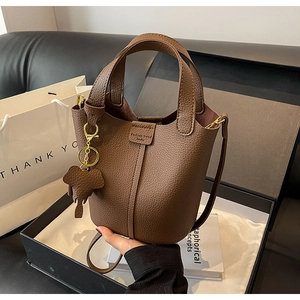Macro detail of brown litchi pattern leather bucket bag with elephant charm in gift box