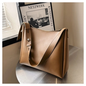 Detail of a brown leather bucket bag with wide shoulder strap and silver metal buckle