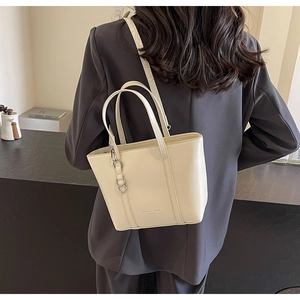 Detailed view of cream leather tote bag with gold logo worn by model in grey suit