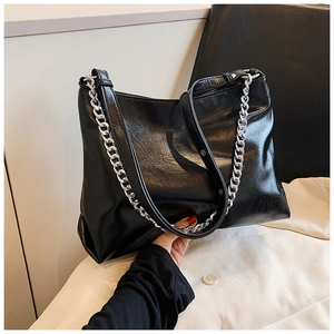 Detail of black glossy tote bag featuring a chunky silver chain and textured soft leather