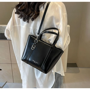 Detail of black glossy tote bag with silver ring accent and adjustable shoulder strap